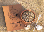 Globe Garden kit with sand, pebbles, and tools on a textured surface