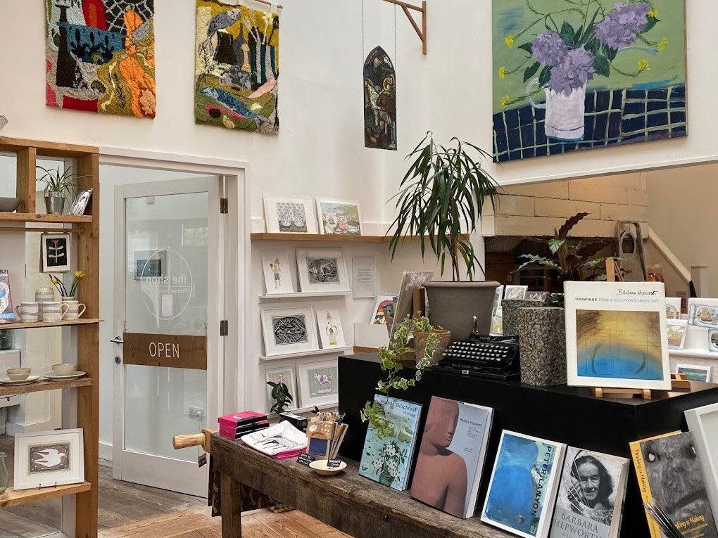 Inside the Shop at Tremenheere: shelves of Cornish ceramics, framed prints and cards by the OPEN door, with contemporary art on the walls